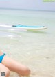 A woman in a blue bikini sitting on the beach next to surfboards.