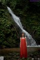 A woman in a red dress standing in front of a waterfall.