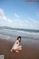 A woman kneeling on a beach next to the ocean.