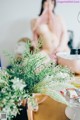 A naked woman sitting at a table with flowers in front of her.