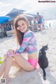 A woman sitting on a beach next to a black cat.