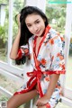 A woman in a red and white floral robe posing by a window.