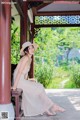 A woman in a white dress and hat sitting on a bench.