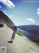 A woman standing on a dirt road next to a lake.