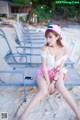 A woman sitting on a beach next to a row of lounge chairs.