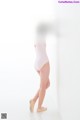 A young girl in a pink leotard leaning against a wall.