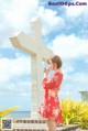 A woman in a red dress standing next to a white cross.