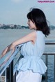 A woman in a blue dress standing on a railing by the water.