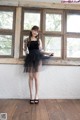 A woman standing in front of a window wearing a black dress.