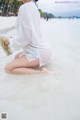 A woman sitting on the beach with her feet in the water.