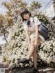 A woman sitting on a wall of white flowers.