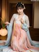 A woman in a pink and blue hanbok sitting on a bed.