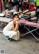 A woman sitting on the ground in front of a table full of hats.