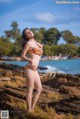 A woman in an orange bikini standing on a rocky beach.